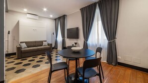 Ein modernes Zimmer mit einer Couch, einem runden Tisch mit Stühlen, einem Flachbildfernseher und einem gemusterten Teppich.