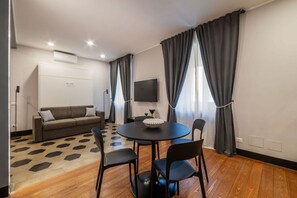 Ein modernes Zimmer mit einer Couch, einem runden Tisch mit Stühlen, einem Flachbildfernseher und einem gemusterten Teppich.