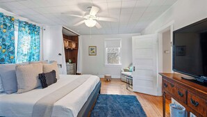 A bedroom with a bed, a ceiling fan, a television, and a window with blinds. - Grandmas House Timeless Charm (Covington)
