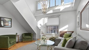 Un loft moderno con una mesa de centro de vidrio, sillones verdes, un sofá gris y un ventanal que deja entrar luz natural.