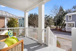 A covered porch with white railings, a wicker chair, and a cushion. - Boutique Downtown Cottage with Golf Cart (Ocean Springs)