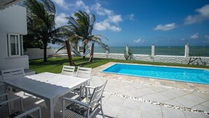 A poolside area with a white table and chairs, a hammock, and palm trees. - Casa do Sol by Carpediem (Ceara-Mirim)