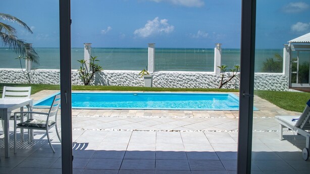 A pool with a view of the ocean, a stone wall, and a white fence. - Casa do Sol by Carpediem (Ceara-Mirim)