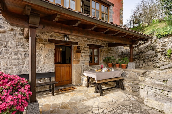 Un bâtiment en pierre avec un banc et une table en bois à l’extérieur, une porte portant l’inscription « TEK » et des plantes en pot.