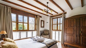 Ein Schlafzimmer mit einem großen Bett, Holzbalken, einem Sessel und einem Kleiderschrank.