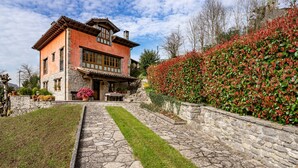 Ein gepflasterter Weg führt zu einem rustikalen Haus mit einer Steinmauer und einem gepflegten Garten.