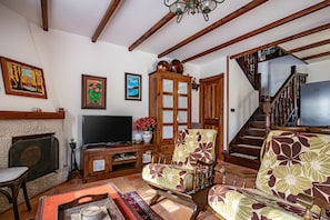 Un salon avec une cheminée, un téléviseur, des meubles en bois et un escalier.