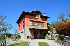 Ein zweistöckiges Steinhaus mit roter Fassade, einem Balkon und einer Steintreppe, die zum Eingang führt.