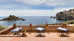 A terrace with a view of the sea, featuring a table and chairs, a potted plant, and a decorative railing. - Il Pescatore Elegant Apartment with Stunning Balcony on Isola Bella, Taormina (Mazzarò)