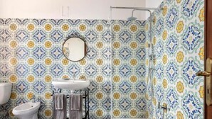 A bathroom with a patterned tile wall, a round mirror, a sink, a bidet, and a shower. - Il Pescatore Elegant Apartment with Stunning Balcony on Isola Bella, Taormina (Mazzarò)