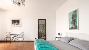 A bedroom with a bed, a desk with chairs, a chandelier, and artwork on the walls. - Il Pescatore Elegant Apartment with Stunning Balcony on Isola Bella, Taormina (Mazzarò)