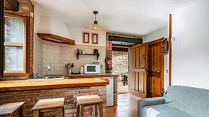 Une cuisine avec un comptoir en bois, un four à micro-ondes et un évier. On y trouve un mur en pierre et des armoires en bois.