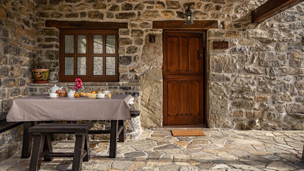 Une façade en pierre avec une porte en bois, une fenêtre à vitres dépolies et une table dressée pour le petit-déjeuner.