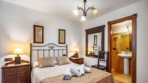 Une chambre à coucher avec un lit, deux tables de chevet avec des lampes, un miroir et une salle de bain visible à travers une porte ouverte.