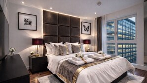 Een moderne slaapkamer met een groot bed, twee nachtkastjes met lampen, uitzicht op een stadsgezicht door grote ramen en kunstwerken aan de wanden.