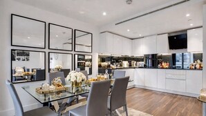 Een moderne keuken met witte kasten, een glazen eettafel en een flatscreen televisie boven de aanrecht.