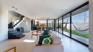 Ein modernes Wohnzimmer mit einer Couch, einem Couchtisch und einem Essbereich mit Stühlen und Tisch. Eine Treppe führt auf eine obere Ebene.