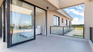 Ein moderner Balkon mit Glastür zu einem Schlafzimmer, Glasgeländer und freiem Blick auf den Himmel.