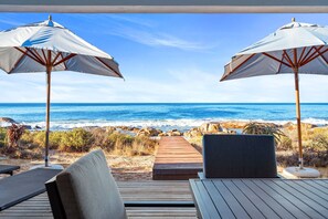 Eine Terrasse am Strand mit zwei Sonnenschirmen, einem Holzdeck und Blick auf das Meer.
