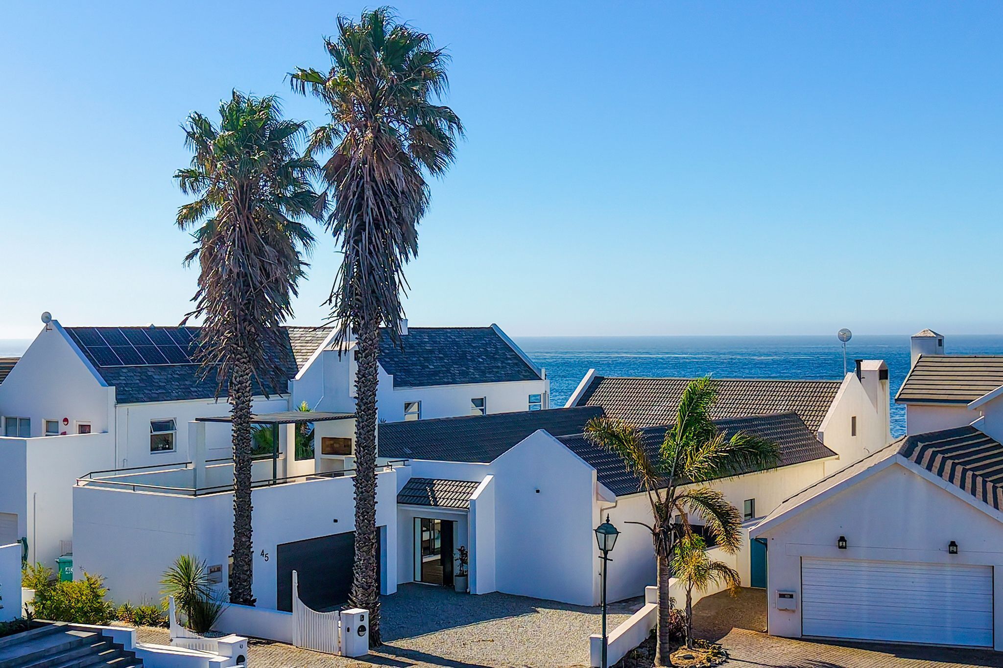 A coastal residential area with white houses, palm trees, and a view of the sea.