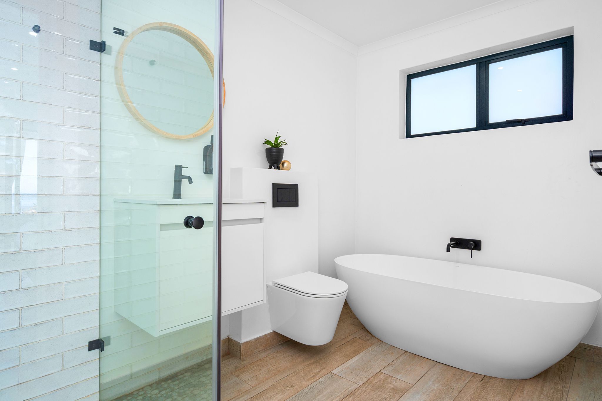 A modern bathroom with a glass shower enclosure, a freestanding toilet, and a large freestanding bathtub.