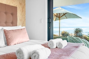 Ein Hotelzimmer mit einem großen Bett, Blick auf den Strand und einem Sonnenschirm vor dem Fenster.