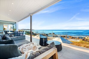 Ein moderner Außenbereich mit einer Couch, einem Esstisch und Stühlen, mit Blick auf eine felsige Küstenlinie und das Meer.