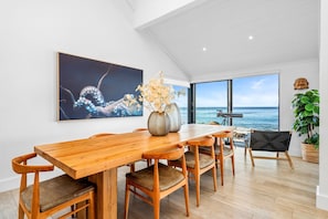 A dining area with a wooden table and chairs, a large painting, and a view of the ocean.
