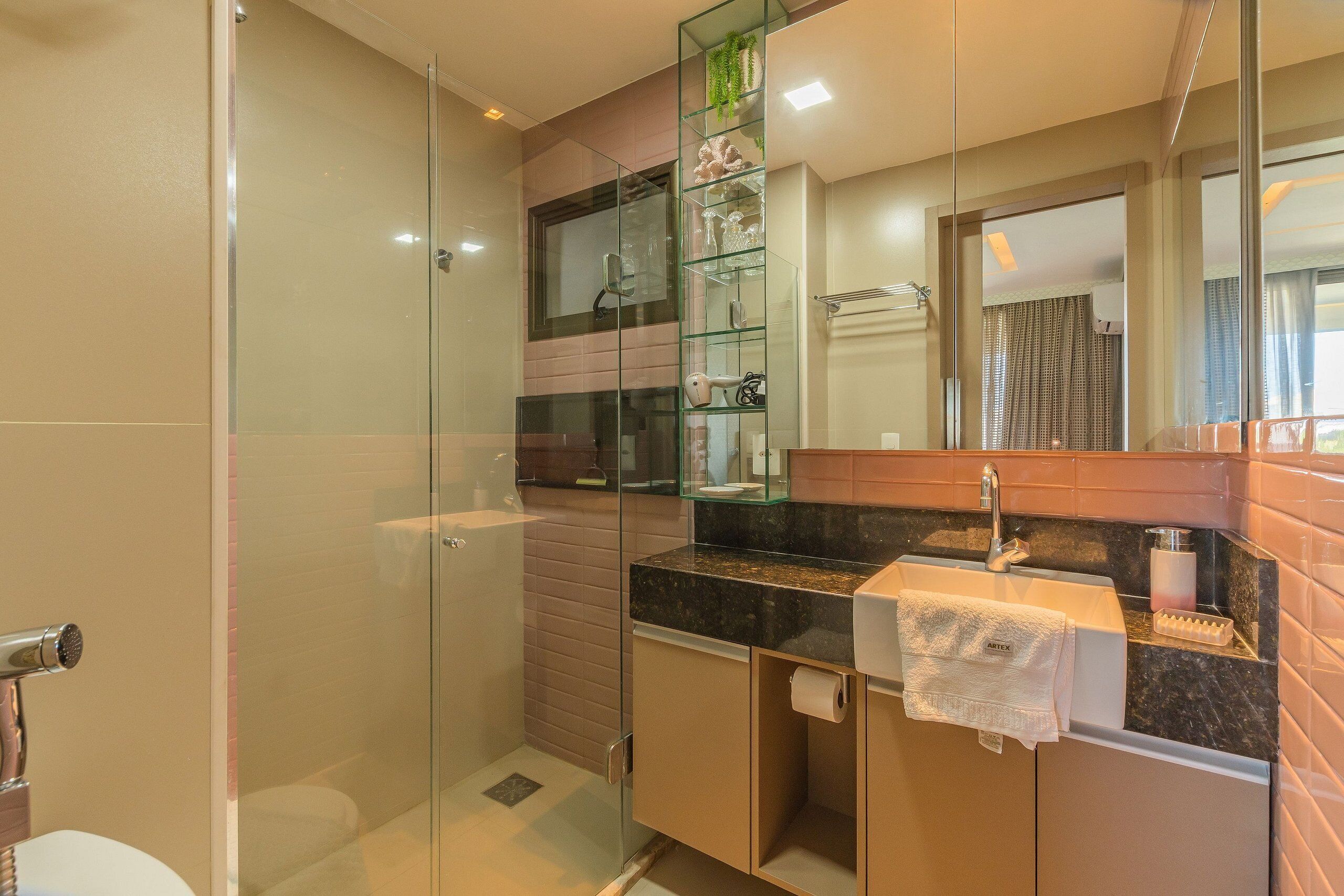 Un baño moderno con ducha de mampara de vidrio, lavabo sobre encimera de mármol y estante de vidrio.