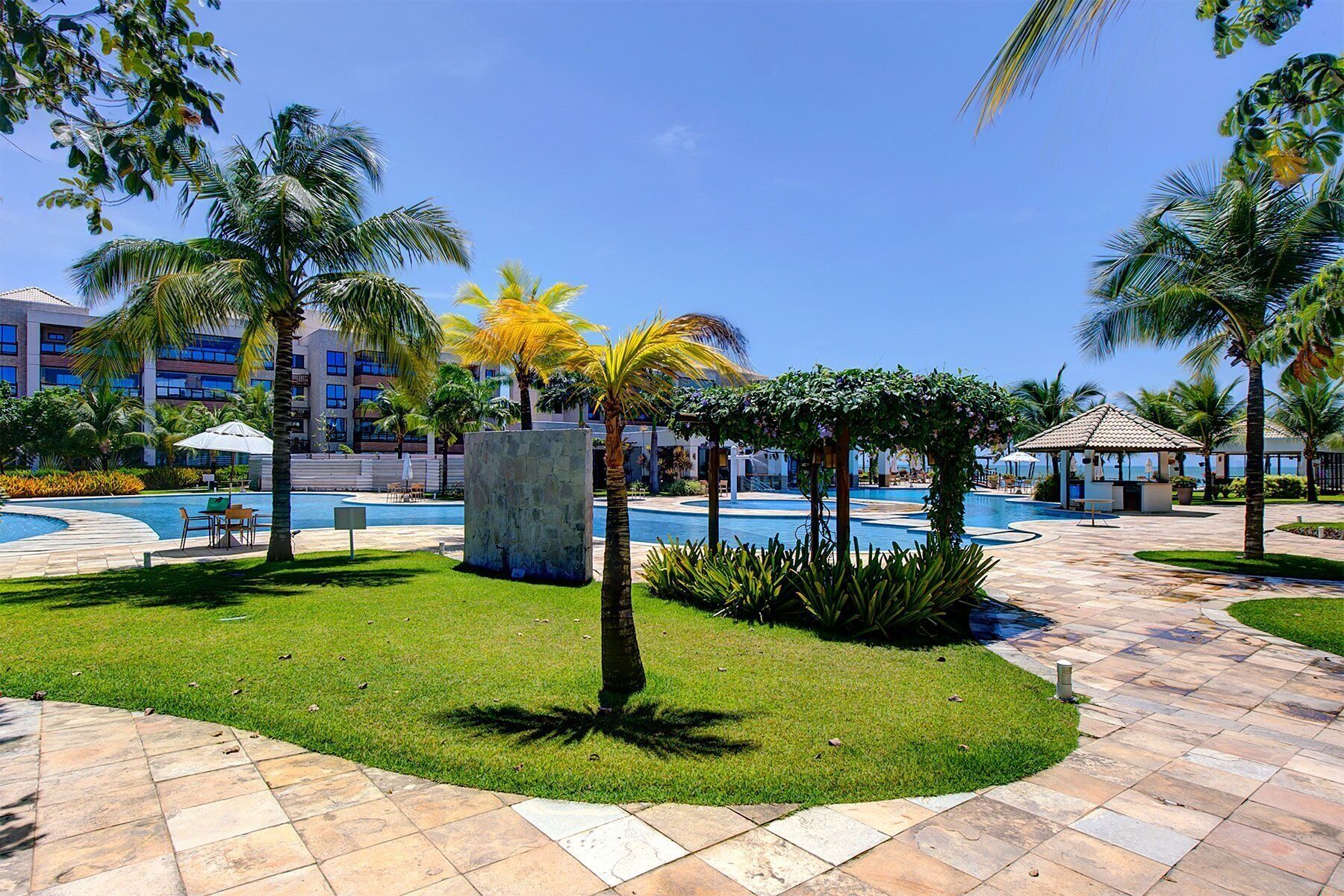 A resort pool area with palm trees, a stone fountain, and a building in the background.