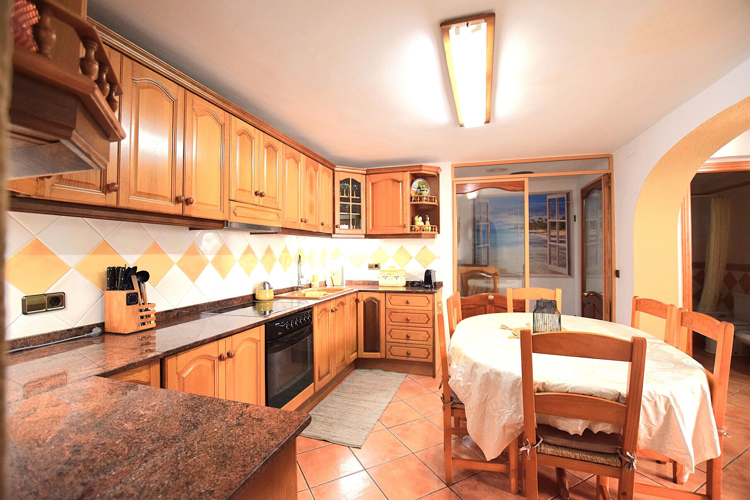 Una cocina con armarios de madera, encimera de granito, una mesa de comedor con sillas y vistas a través de un ventanal.