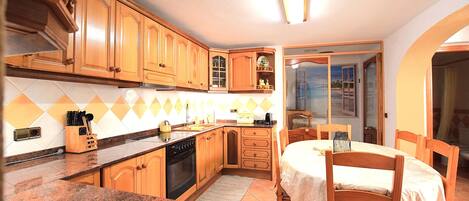 Una cocina con armarios de madera, encimera de granito, una mesa de comedor con sillas y vistas a través de un ventanal.