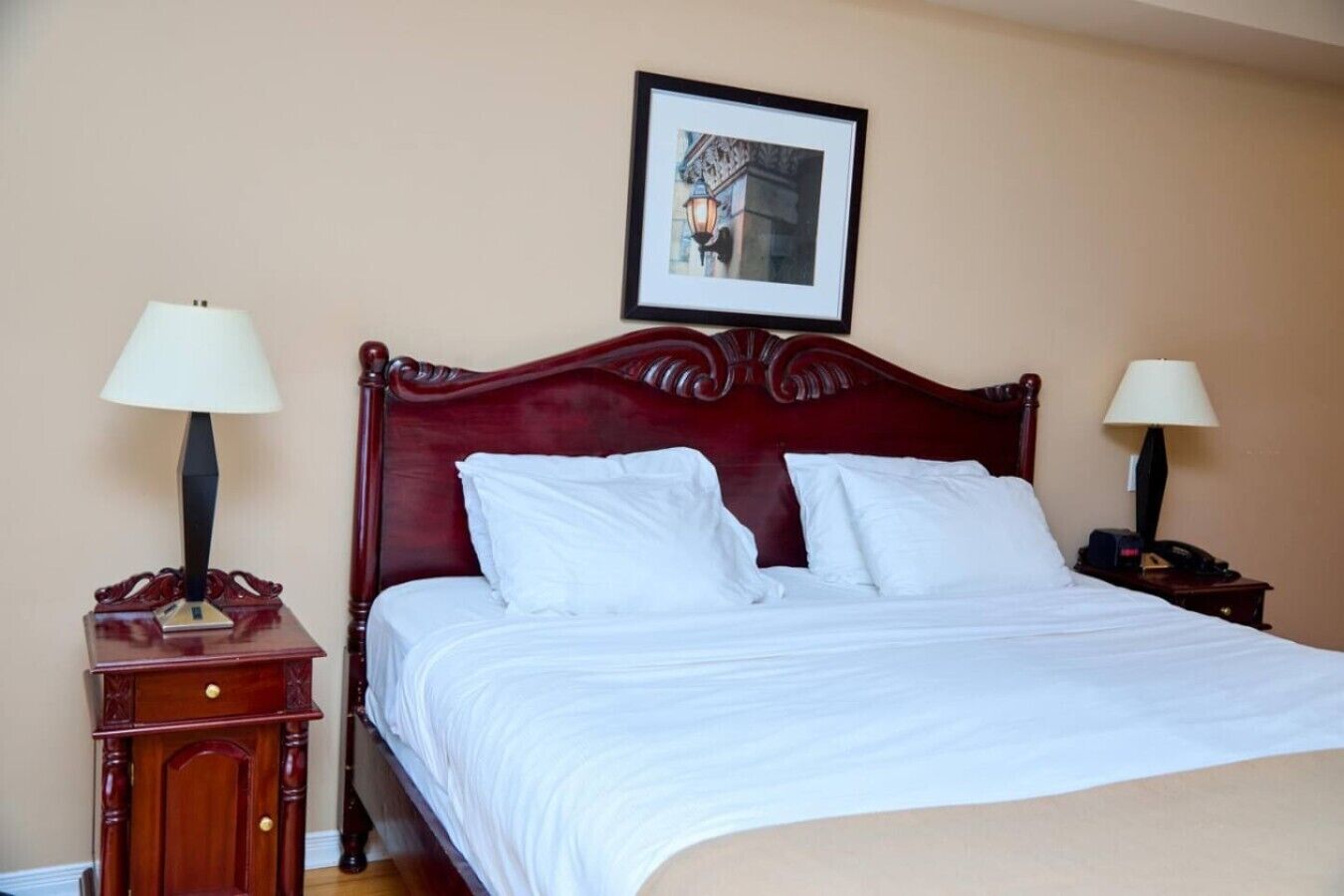 A neatly made bed with white linens, two bedside tables with lamps, and a framed picture on the wall.