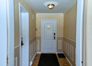A hallway with a white door, a black doormat, and a light fixture on the ceiling.