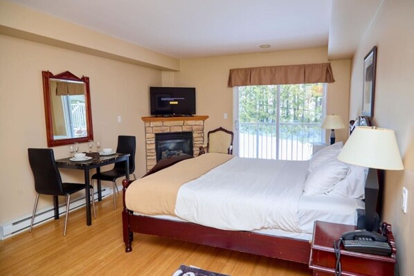 A hotel room with a bed, a desk with chairs, a television, a fireplace, and a window with a view.
