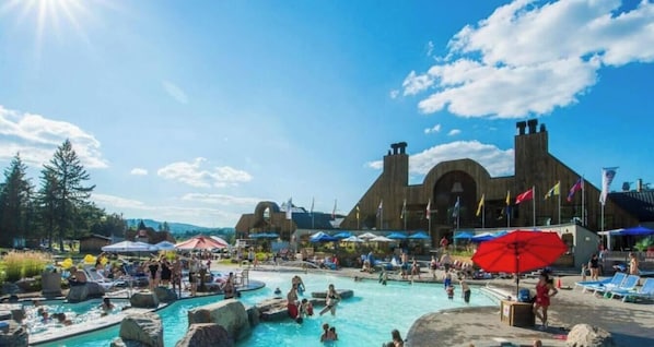 Un complexe hôtelier doté d’une vaste piscine, d’un bâtiment en bois aux fenêtres en arc de cercle et de nombreux drapeaux.