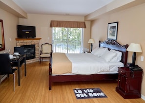 Habitación de hotel con cama, televisor, chimenea, zona de comedor y ventana con vistas.