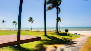 A wooden deck leading to a beach with palm trees and a clear view of the ocean. - Wai Wai #a406 - Beachfront Resort By Carpediem (Caucaia)