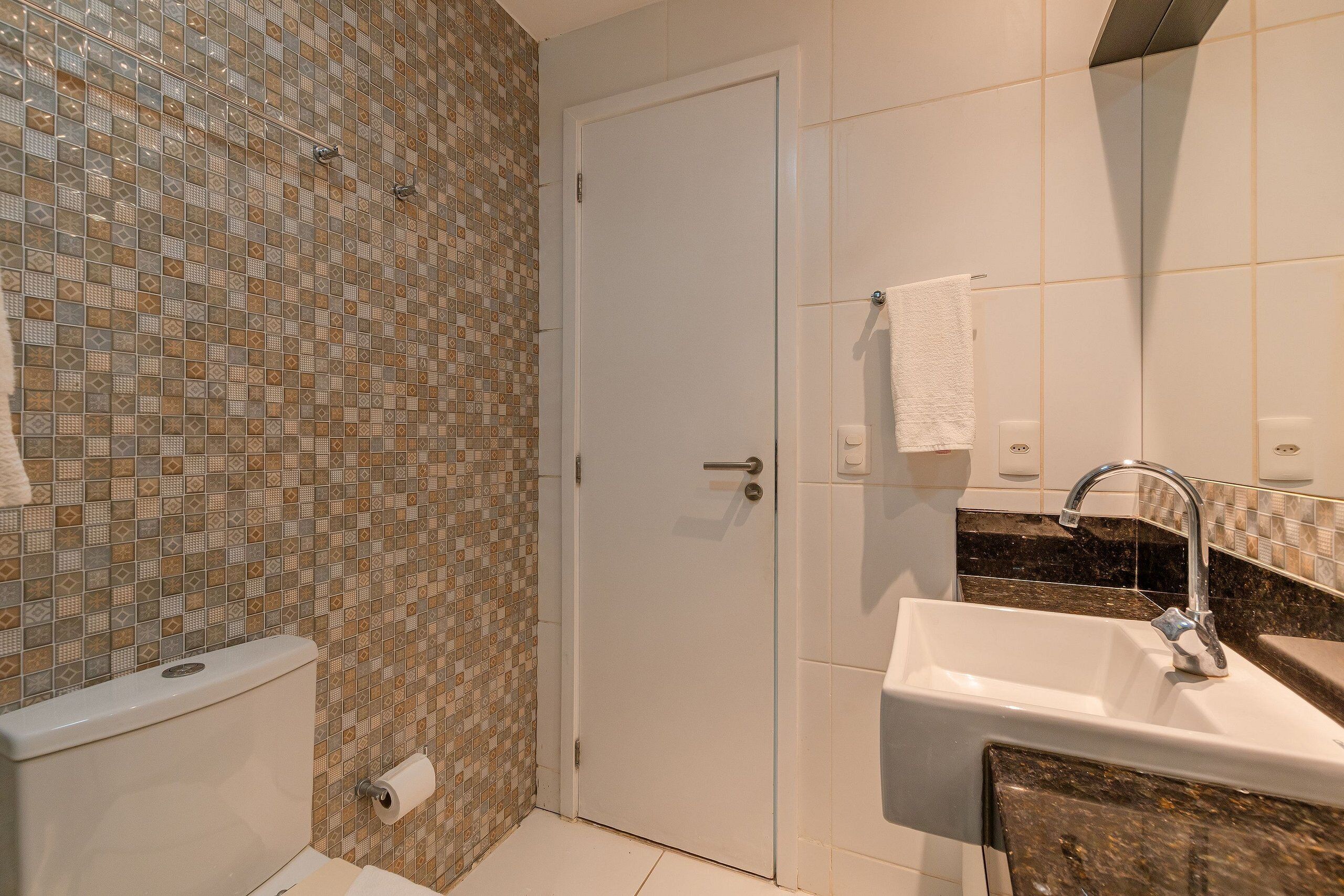 A bathroom with a tiled wall, a toilet, a sink with a mirror, and a towel hanging on the wall.