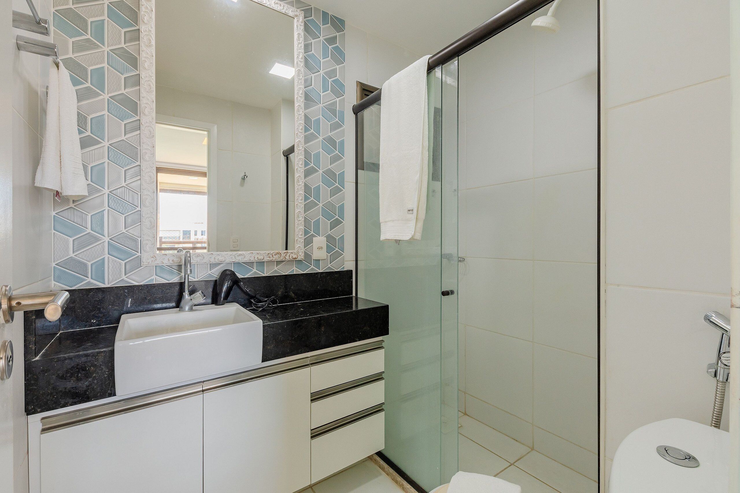 A modern bathroom with a glass shower enclosure, a white sink with a black countertop, and a tiled backsplash.