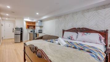 A bedroom with a wooden bed, a small kitchenette, and a herringbone-patterned wall.