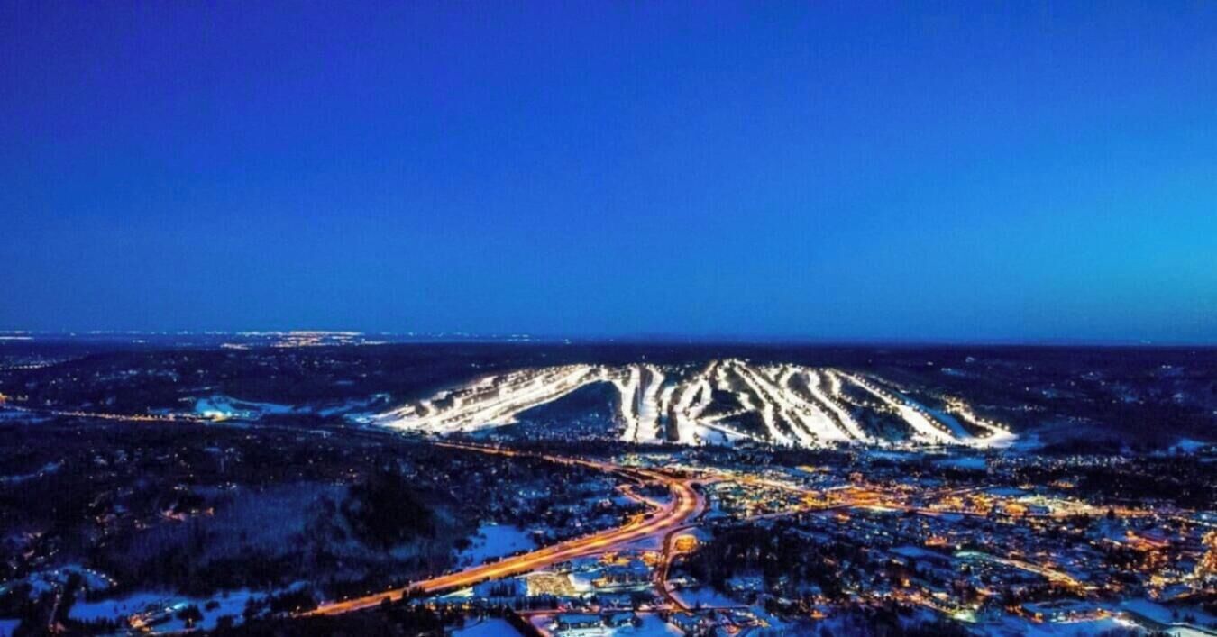 A nighttime aerial view of a city with a prominent mountain in the background.