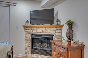 Una sala de estar con una chimenea de piedra, un televisor de pantalla plana montado arriba y un mueble de madera con cajones.