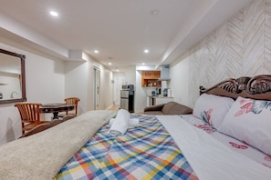A hotel room with a bed, a desk, a chair, a kitchenette, and a bathroom.