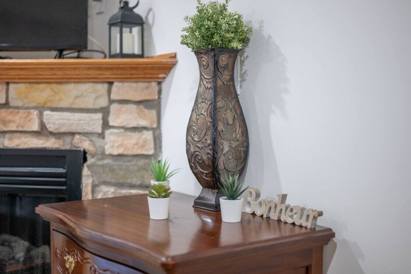 A wooden table with a decorative vase and two small potted plants.