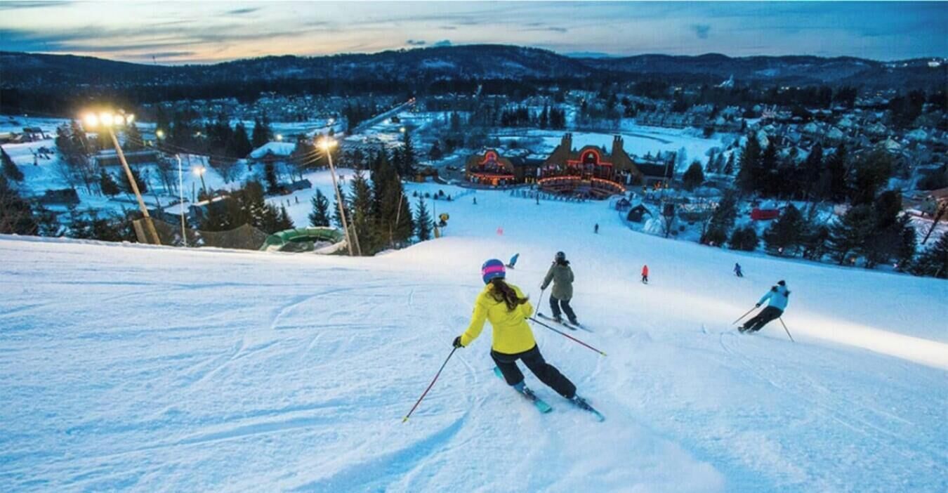 A ski slope with skiers, a town in the background, and a hotel named Sommet Saint-Sauveur.