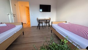 A hotel room with two beds, a desk, a chair, a television, and a potted plant. - Vacation apartment 6 persons, near Cloppenburg, bedroom with TV and single beds (Cappeln (Oldenburg))