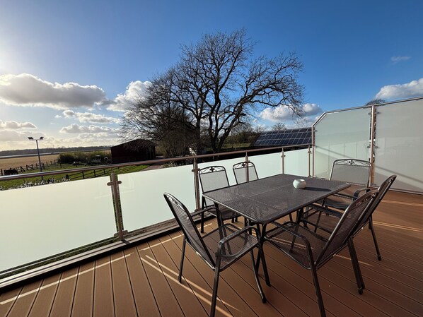 Une terrasse avec une table et des chaises, donnant sur une rivière et des champs.