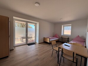 Une pièce avec un plancher en bois, un lit recouvert d’une couette à carreaux rouges et blancs, un bureau avec une chaise et une fenêtre avec des stores.