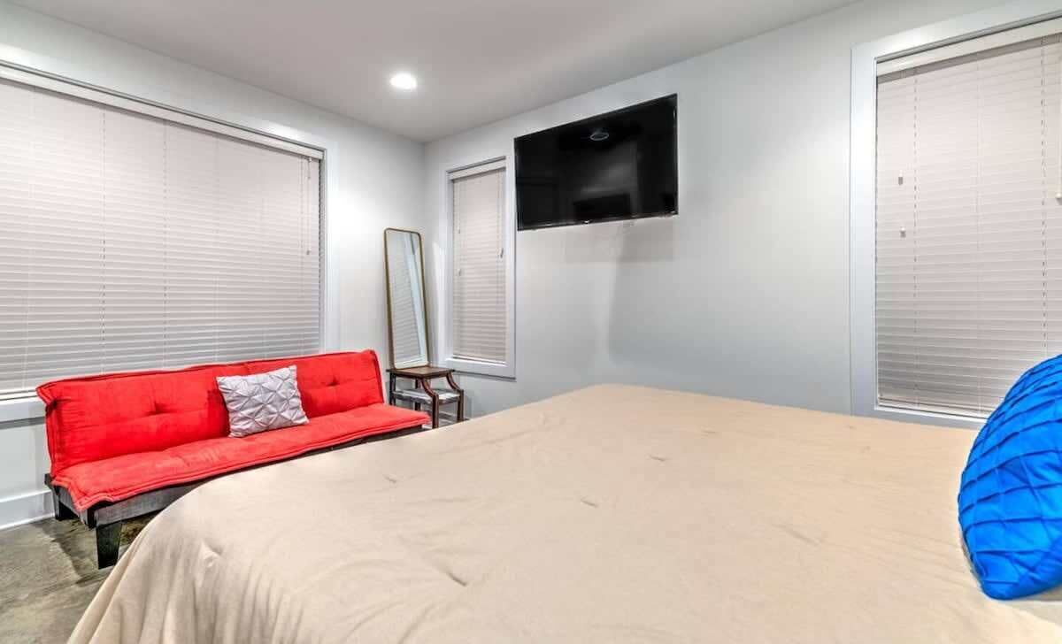 Une chambre à coucher avec un lit, un canapé rouge, une petite table et un téléviseur fixé au mur.